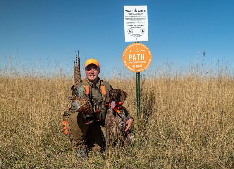 Hunter in field with dog next to PATH sign