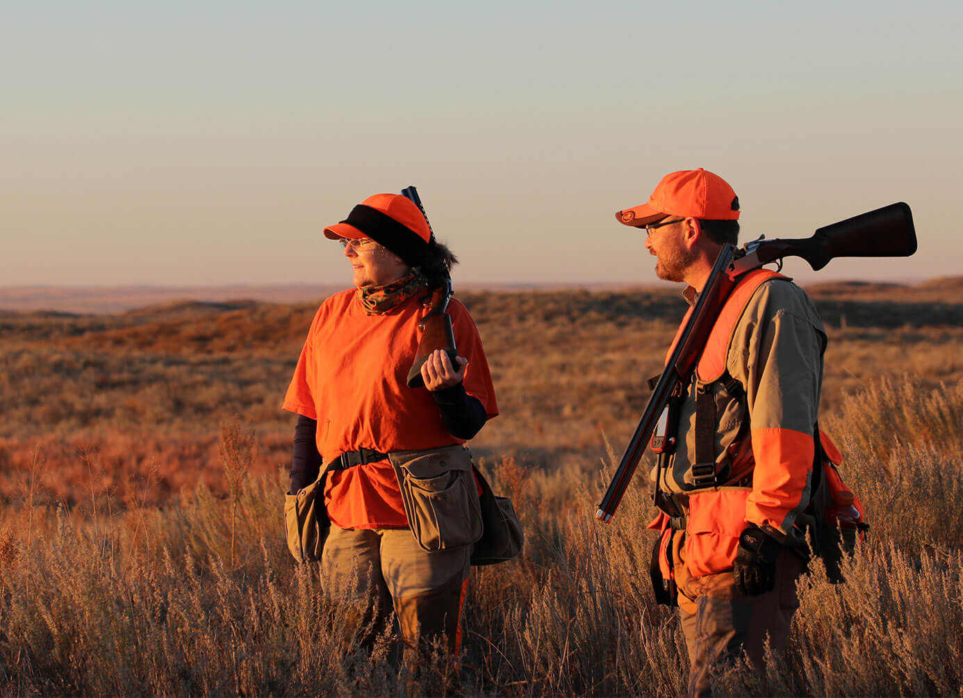 Two hunter in field looking toward a sunset