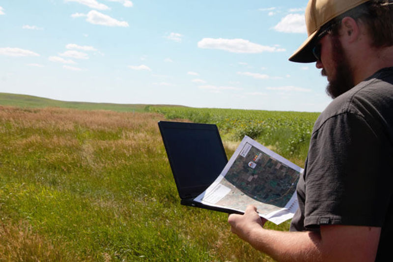 Field worker in field with laptop and print out